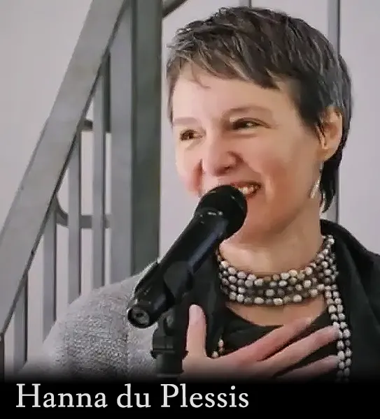 Picture of Hanna du Plessis, smiling woman with short dark hair in a gray sweater with a necklace of beads, speaking at a microphone